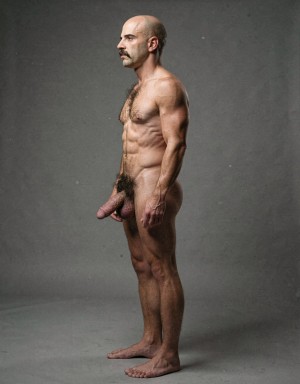 Mike Morris, a 32-year-old extremely lean Caucasian male with only 8% body fat, stands completely naked in a strict military attention pose captured in a full-body exact side profile at 90 degrees from his left side. The shot runs from the tips of his size 44 slightly hairy feet all the way up to the top of his bald head, showing his entire body without any cropping. His physique is dry, highly vascular and powerfully defined: massive square pectorals seen in perfect side silhouette, dense dark brown chest hair forming a thick T-pattern, sharply carved six-pack abs in clear profile, narrow waist, wide lats, powerful thighs and diamond-shaped calves. Dramatic directional studio lighting comes from high and slightly in front of him, creating strong rim lighting that traces the sharp outline of his entire body, the texture of his dense dark body hair on chest, lower back, ass and legs, and deep shadows that accentuate every muscle separation, vein and the extreme dryness of his 8% body fat physique. His advanced Norwood III-IV bald scalp shines under the light, with short dense dark brown hair on the sides and back of his head. His square angular face is shown in pure profile: strong jawline, prominent chin with slight central dimple, thick dark handlebar mustache, heavy brow and intense deep-set brown eye looking straight forward with a serious, commanding expression. His penis is fully visible in perfect side view, completely natural and realistic: thick, 24 cm long when fully erect, with a natural slight upward curve, prominent dorsal veins, long foreskin partially covering the pink-red glans, and realistic lighter skin tone. Below it hang his large, low-hanging testicles with wrinkled darker skin and dense dark brown hair. The extremely thick, curly dark brown pubic bush climbs almost to his navel and surrounds the base of his cock and balls generously. Every anatomical detail from his veined hands and forearms to his muscular ass, hamstrings, diamond calves and hairy toes is perfectly proportioned and free of any deformation. Photorealistic, high-contrast, masculine 1970s Colt Studio aesthetic with subtle grainy film texture.