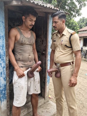 Dos hombres de pie junto a la entrada de una pequeña construcción rural con paredes azules desgastadas y tejado de chapa; a la izquierda, un hombre con camiseta de tirantes sucia y pantalón corto blanco mira hacia abajo mientras sostiene con una mano un pene grande y flácido que sobresale por delante, en una escena de aspecto crudo y descuidado. A la derecha, un policía con uniforme caqui, cinturón marrón, charreteras y bolígrafos en el bolsillo observa seriamente al otro hombre, con otro pene exageradamente grande visible fuera del pantalón, colgando sobre la zona de la bragueta. El entorno parece un patio de tierra con vegetación, una bicicleta al fondo y edificios sencillos, creando un contraste llamativo entre la autoridad policial, la pobreza del lugar y el contenido sexual explícito.