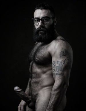 Fotografía hiperrealista en blanco y negro de un hombre adulto musculoso a la vista desde las rodillas para arriba hasta la cabeza, cuerpo muy delgado con musculación marcada y definida, rostro masculino, totalmente desnudo con polla erecta de treinta centímetros de longitud y ocho centímetros de diámetro, tiene rasgos marcados duros expresivos, barba densa poblada tupida oscura estilo hipster cubriendo completamente mandíbula mentón mejillas con grosor uniforme textura abundante muy definida, bigote denso tupido oscuro conectado perfectamente con la barba completa cubriendo completamente el labio superior, pelo oscuro medio peinado completamente recto hacia arriba con volumen considerable estilo hipster moderno quiff puntas verticales texturizadas hacia el cielo con altura prominente, cejas gruesas oscuras pobladas muy marcadas definidas, gafas de montura completa negra cuadradas grandes estilo hipster moderno sobre el puente de la nariz enmarcando unos ojos oscuros intensos que miran directamente a cámara con expresión seria penetrante confiada, expresión facial seria masculina sin sonrisa con mirada directa desafiante, pómulos marcados definidos angulares, nariz recta proporcionada, labios medios apenas visibles completamente cubiertos por bigote denso que conecta con la barba hipster completa, torso desnudo muy musculoso con pectorales enormes desarrollados y definidos, hombros anchos musculosos deltoide prominentes, brazos musculosos gruesos con bíceps y tríceps marcados visibles a ambos lados del cuerpo, abdomen tonificado marcado visible desde la cintura, piel con textura realista detallada poros imperfecciones sutiles, vello corporal denso oscuro abundante cubriendo pectorales abdomen brazos hombros con textura natural masculina muy visible, tatuaje en tinta negra en el bíceps del brazo derecho con la palabra exacta 