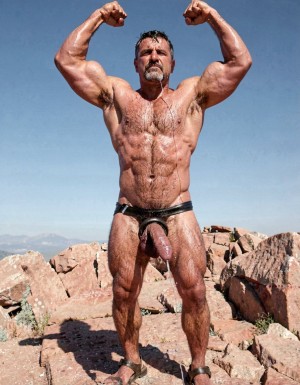 A hyper-masculine ancient Zapotec warrior named Cocijo, 26 years old, standing perfectly still under the brutal midday sun on the rocky summit of Cerro La Cantera in San Pablo Huitzo, Oaxaca, 600 AD. Completely naked except for worn leather strip sandals. Square jaw clenched, thick veiny neck, bronze skin drenched in sweat. Extremely powerful and fully flexed physique: massive square pectorals tensed to the maximum, thick dark wet chest hair matted against the hard muscle, large erect nipples. Deeply carved eight-pack abs glistening with sweat, thick black treasure trail running down to a dense dark pubic bush. Enormous arms raised and flexed hard overhead, biceps bulging like cannonballs with thick veins, triceps perfectly defined and tensed like horseshoes. Thick hairy thighs locked in full tension. His massive 35cm cock is rock-hard and throbbing violently, held tightly at the very base by Gayon Von Neumann’s strong hand, the swollen head continuously leaking thick white precum that runs down the shaft and over the fingers. A thick black leather cock ring is locked brutally tight at the root, behind his heavy balls, making the entire package look painfully swollen, darker and pulsing non-stop. Cocijo stares straight up with total obedience, every muscle in his body still tensed and displayed for inspection. Raw, dominant, extremely virile ancient masculine atmosphere, dramatic sunlight casting strong shadows on every ridge of muscle, hyper-realistic and extremely detailed.