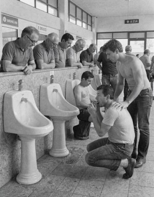 Madrid, 1985. Dentro del edificio la estación autobuses hay unos urinarios de loza de pedestal (van del suelo a un metro de altura), varios hombres casados orinan mostrando sus penes erectos visibles, un chico joven se acerca y mira con lascivia, el chico está arrodillado y practica una felación a uno de los hombres que orinan. Varios mirones apoyados en un murete observan la escena con envidia. 
