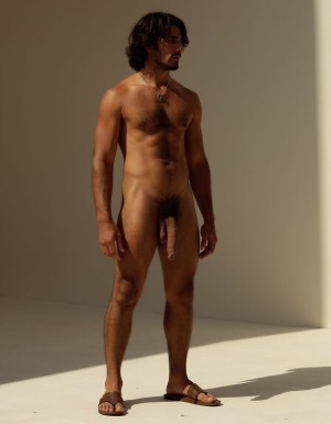 Hombre con piel bronceada desnudo que tiene un pene de 30 cm de longitud y 4 cm de grueso. Tiene dos testículos grandes gruesos peludos hermosos que cuelgan mucho. Tiene cabello oscuro y largo. Tiene sandalias marrones. Tiene músculos pectorales peludos. 🧔🏻‍♂️ 🌷🥀🌹☀️🌈 🏜️ hombre muy delgado