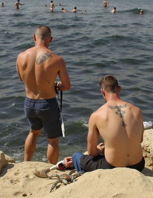 Robados. 
Supuesto "robado" de dos pescadores heteros de treinta y cinco años de espaldas, llevan pantalón corto, han echado la caña al agua y muestran sus anchas espaldas tatuadas, al fondo se ven los bañistas de la cala del Racó del Conil en Alicante