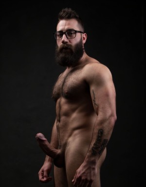 Fotografía hiperrealista de un hombre adulto musculoso a la vista desde los pies para arriba hasta la cabeza, tiene cuerpo muy delgado con músculos marcados y definidos, rostro masculino idéntico a la imagen de referencia, está totalmente desnudo con polla erecta de treinta centímetros de longitud y ocho centímetros de diámetro, tiene rasgos marcados duros expresivos, barba densa poblada tupida oscura estilo hipster cubriendo completamente mandíbula mentón mejillas con grosor uniforme textura abundante muy definida, bigote denso tupido oscuro conectado perfectamente con la barba completa cubriendo completamente el labio superior, pelo oscuro medio peinado completamente recto hacia arriba con volumen considerable estilo hipster moderno quiff puntas verticales texturizadas hacia el cielo con altura prominente, cejas gruesas oscuras pobladas muy marcadas definidas, gafas de montura completa negra cuadradas grandes estilo hipster moderno sobre el puente de la nariz enmarcando unos ojos oscuros intensos que miran directamente a cámara con expresión seria penetrante confiada, expresión facial seria masculina sin sonrisa con mirada directa desafiante, pómulos marcados definidos angulares, nariz recta proporcionada, labios medios apenas visibles completamente cubiertos por bigote denso que conecta con la barba hipster completa, torso desnudo muy musculoso con pectorales enormes desarrollados y definidos, hombros anchos musculosos deltoide prominentes, brazos musculosos gruesos con bíceps y tríceps marcados visibles a ambos lados del cuerpo, abdomen tonificado marcado visible desde la cintura, piel con textura realista detallada poros imperfecciones sutiles, vello corporal denso oscuro abundante cubriendo pectorales abdomen brazos hombros con textura natural masculina muy visible, tatuaje en tinta negra en el bíceps del brazo derecho con la palabra exacta "hipsterbarba" en tipografía negra sans-serif clara legible tatuada sobre la piel del brazo de tamaño mediano visible proporcionado, iluminación dramática lateral direccional que crea contraste alto marcado entre luces brillantes y sombras profundas resaltando la estructura facial angular la barba hipster densa las gafas cuadradas grandes el vello corporal abundante la musculatura del torso los brazos y el tatuaje con la palabra "hipsterbarba" en el bíceps derecho, fondo completamente oscuro negro liso uniforme desenfocado sin distracciones, fotografía analógica en color de alto contraste con grano fotográfico sutil visible estilo retrato hipster masculino fitness, enfoque nítido absoluto perfecto en el rostro especialmente en los ojos detrás de las gafas la barba hipster densa el bigote tupido el pelo vertical el vello corporal el torso musculoso y el tatuaje con la palabra "hipsterbarba" en el brazo derecho, encuadre vertical desde la cintura hacia arriba mostrando completamente todo el torso superior los brazos musculosos y la cabeza, calidad fotográfica hiperrealista 8K máxima definición detalle extremo, renderizado cinematográfico fotorrealista profesional.