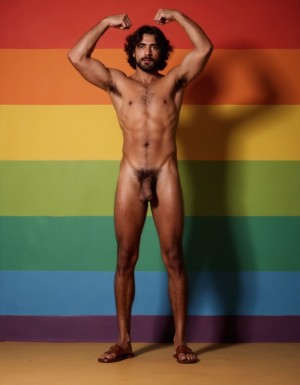 Hombre con piel bronceada desnudo que tiene un pene de 30 cm de longitud y 4 cm de grueso. Tiene dos testículos grandes de 10 cm de diámetro gruesos y peludos hermosos que cuelgan mucho. Tiene cabello oscuro y largo. Tiene sandalias marrones. Tiene músculos pectorales peludos. hombre delgado muy viril muy macho, fondo 🌈. Tiene los brazos flexionados doblados hacia arriba con fuerza para mostrar sus fuertes músculos bíceps y tríceps de sus brazos 