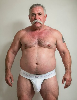 Un hombre de sesenta años, con una constitución fuerte y robusta, pesando 140 kilos, presenta una barriga impresionante y prominente, con un contorno redondeado que se extiende por debajo de su cintura. Su rostro está adornado con un bigote estilo Dalí, grueso y bien definido, de color blanco, que le confiere un aire de distinción y elegancia. Viste slips blancos ajustados que marcan claramente la silueta de su pene, que aunque es pequeño, tiene un grosor notable y se erige con confianza. La ausencia de camiseta permite apreciar su torso peludo, con un vello abundante y blanco que cubre su pecho y abdomen, resaltando su masculinidad y edad madura. Su piel es suave y arrugada, con una textura que refleja su edad y experiencia. La imagen debería ser hiperrealista, con detalles de alta calidad, capturando la textura de su piel, el brillo de su bigote blanco y la suavidad de su vello corporal. La iluminación debería ser suave, con sombras que realcen la forma de su cuerpo y resalten su presencia imponente, destacando su peso y su volumen. El fondo debería ser neutro, para que el hombre sea el centro de atención, y su presencia llene todo el espacio. El estilo de la imagen debería ser fotográfico, con un enfoque en la realidad y la autenticidad, sin elementos distractores o artificiales. La imagen debería transmitir una sensación de confianza y seguridad, como si el hombre estuviera disfrutando de su propia compañía y de su cuerpo maduro y fuerte.