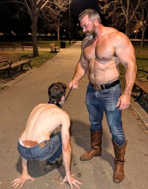 macho de 22 años en posición de cuatro patas, de cuerpo muy delgado y completamente desnudo, enseñando su culo abierto en primer plano. Con un gran collar de cuero negro. A su lado de pie un maduro de 55 años con barba, de brazos grandes y fuertes, complexión fuerte y vello en su cuerpo. Lleva un pantalón vaquero ajustado marcando su gran pene. Lleva un cinturón con gran hebilla y unas botas vaqueras. El maduro mira con vicio el culo abierto y húmedo del macho de 22 años, mientras sujeta la correa  en la mano que tiene el collar del macho de 22 años. Están en un parque publico vacío de noche con asientos y caminos por el parque.