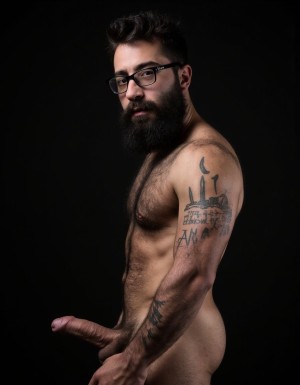 Fotografía hiperrealista de un hombre adulto musculoso pero muy delgado a la vista desde las rodillas para arriba hasta la cabeza, cuerpo muy delgado pero con musculación marcada y definida, rostro masculino idéntico a la imagen de referencia totalmente desnudo con polla erecta de treinta centímetros de longitud y ocho centímetros de diámetro, tiene rasgos marcados duros expresivos, barba densa poblada tupida oscura estilo hipster cubriendo completamente mandíbula mentón mejillas con grosor uniforme textura abundante muy definida, bigote denso tupido oscuro conectado perfectamente con la barba completa cubriendo completamente el labio superior, pelo oscuro medio peinado completamente recto hacia arriba con volumen considerable estilo hipster moderno quiff puntas verticales texturizadas hacia el cielo con altura prominente, cejas gruesas oscuras pobladas muy marcadas definidas, gafas de montura completa negra cuadradas grandes estilo hipster moderno sobre el puente de la nariz enmarcando unos ojos oscuros intensos que miran directamente a cámara con expresión seria penetrante confiada, expresión facial seria masculina sin sonrisa con mirada directa desafiante, pómulos marcados definidos angulares, nariz recta proporcionada, labios medios apenas visibles completamente cubiertos por bigote denso que conecta con la barba hipster completa, torso desnudo muy musculoso con pectorales enormes desarrollados y definidos y velludos peludos, hombros anchos musculosos deltoide prominentes, brazos musculosos gruesos con bíceps y tríceps marcados visibles a ambos lados del cuerpo, abdomen tonificado marcado visible desde la cintura, piel con textura realista detallada poros imperfecciones sutiles, vello corporal denso oscuro abundante cubriendo pectorales abdomen brazos hombros con textura natural masculina muy visible, tatuaje en tinta negra en el bíceps del brazo derecho con la palabra exacta (("hipsterbarba")) en tipografía negra sans-serif clara legible tatuada sobre la piel del brazo de tamaño mediano visible proporcionado, iluminación dramática lateral direccional que crea contraste alto marcado entre luces brillantes y sombras profundas resaltando la estructura facial angular la barba hipster densa las gafas cuadradas grandes el vello corporal abundante la musculatura del torso los brazos y el tatuaje con la palabra (("hipsterbarba")) en el bíceps derecho, fondo completamente oscuro negro liso uniforme desenfocado sin distracciones, fotografía de alto contraste con grano fotográfico sutil visible estilo retrato hipster masculino fitness, enfoque nítido absoluto perfecto en el rostro especialmente en los ojos detrás de las gafas la barba hipster densa el bigote tupido el pelo vertical el vello corporal el torso musculoso y el tatuaje con la palabra "hipsterbarba" a la vista en el brazo derecho, encuadre vertical desde la cintura hacia arriba mostrando completamente todo el torso superior los brazos musculosos y la cabeza, calidad fotográfica hiperrealista 8K máxima definición detalle extremo, renderizado cinematográfico fotorrealista profesional. Está totalmente desnudo. Palabra “hipsterbarba” a la vista tatuada en el pectoral derecho.