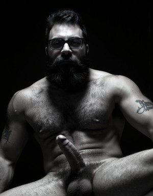 Fotografía hiperrealista en blanco y negro de un hombre adulto musculoso a la vista desde las rodillas para arriba hasta la cabeza, cuerpo muy delgado con musculación marcada y definida, rostro masculino, totalmente desnudo con polla erecta de treinta centímetros de longitud y ocho centímetros de diámetro, tiene rasgos marcados duros expresivos, barba densa poblada tupida oscura estilo hipster cubriendo completamente mandíbula mentón mejillas con grosor uniforme textura abundante muy definida, bigote denso tupido oscuro conectado perfectamente con la barba completa cubriendo completamente el labio superior, pelo oscuro medio peinado completamente recto hacia arriba con volumen considerable estilo hipster moderno quiff puntas verticales texturizadas hacia el cielo con altura prominente, cejas gruesas oscuras pobladas muy marcadas definidas, gafas de montura completa negra cuadradas grandes estilo hipster moderno sobre el puente de la nariz enmarcando unos ojos oscuros intensos que miran directamente a cámara con expresión seria penetrante confiada, expresión facial seria masculina sin sonrisa con mirada directa desafiante, pómulos marcados definidos angulares, nariz recta proporcionada, labios medios apenas visibles completamente cubiertos por bigote denso que conecta con la barba hipster completa, torso desnudo muy musculoso con pectorales enormes desarrollados y definidos, hombros anchos musculosos deltoide prominentes, brazos musculosos gruesos con bíceps y tríceps marcados visibles a ambos lados del cuerpo, abdomen tonificado marcado visible desde la cintura, piel con textura realista detallada poros imperfecciones sutiles, vello corporal denso oscuro abundante cubriendo pectorales abdomen brazos hombros con textura natural masculina muy visible, tatuaje en tinta negra en el bíceps del brazo derecho con la palabra exacta "hipsterbarba" en tipografía negra sans-serif clara legible tatuada sobre la piel del brazo de tamaño mediano visible proporcionado, iluminación dramática lateral direccional que crea contraste alto marcado entre luces brillantes y sombras profundas resaltando la estructura facial angular la barba hipster densa las gafas cuadradas grandes el vello corporal abundante la musculatura del torso los brazos y en el bíceps derecho tiene un tatuaje con la palabra a la vista: "hipsterbarba", fondo completamente oscuro negro liso uniforme desenfocado sin distracciones, fotografía analógica en blanco y negro de alto contraste con grano fotográfico sutil visible estilo retrato hipster masculino fitness, enfoque nítido absoluto perfecto en el rostro especialmente en los ojos detrás de las gafas la barba hipster densa el bigote tupido el pelo vertical el vello corporal el torso musculoso y el tatuaje en el brazo derecho con la palabra a la vista "hipsterbarba", encuadre vertical desde las rodillas cintura hacia arriba mostrando pene erecto de treinta centímetros de longitud completamente todo el torso superior los brazos musculosos y la cabeza, calidad fotográfica hiperrealista 8K máxima definición detalle extremo, renderizado cinematográfico fotorrealista profesional.