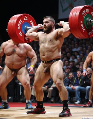 Varios hombre extremadamente musculoso y barbudo en una competición de halterofilia. Se muestra desnudo mientras levanta una enorme barra con pesas de trescientos kilos
