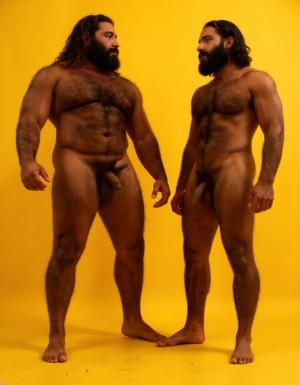 Dos guerreros musculosos delgados y altos, cuerpo completamente desnudo y velludo, mostrando polla venosa de 30 cm de longitud y 5 cm de grosor. Tienen la piel bronceada por el Sol, con pelo muy largo y barba. Tiene pies fuertes. Están contentos. Tienen músculos marcados definidos y sin nada de grasa. Tienen aspecto muy viril. Tienen cuerpo muy delgado pero con los músculos marcados y muy definidos. Están tensos haciendo fuerza para mostrar sus músculos marcados. Fondo amarillo oscuro con los reflejos de las sombras de los cuerpos.