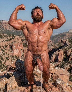A hyper-masculine ancient Zapotec warrior named Cocijo, 26 years old, standing perfectly still under the brutal midday sun on the rocky summit of Cerro La Cantera in San Pablo Huitzo, Oaxaca, 600 AD. Completely naked except for worn leather strip sandals. Square jaw clenched, thick veiny neck, bronze skin drenched in sweat. Extremely powerful and fully flexed physique: massive square pectorals tensed to the maximum, thick dark wet chest hair matted against the hard muscle, large erect nipples. Deeply carved eight-pack abs glistening with sweat, thick black treasure trail running down to a dense dark pubic bush. Enormous arms raised and flexed hard overhead, biceps bulging like cannonballs with thick veins, triceps perfectly defined and tensed like horseshoes. Thick hairy thighs locked in full tension. His massive 35cm cock is rock-hard and throbbing violently, held tightly at the very base by Gayon Von Neumann’s strong hand, the swollen head continuously leaking thick white precum that runs down the shaft and over the fingers. A thick black leather cock ring is locked brutally tight at the root, behind his heavy balls, making the entire package look painfully swollen, darker and pulsing non-stop. Cocijo stares straight up with total obedience, every muscle in his body still tensed and displayed for inspection. Raw, dominant, extremely virile ancient masculine atmosphere, dramatic sunlight casting strong shadows on every ridge of muscle, hyper-realistic and extremely detailed.