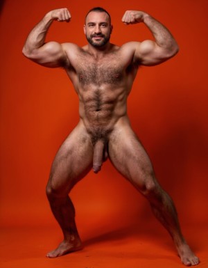 hombre culturista de 35 años posando desnudo de cuerpo completo, sonriente, tensa los bíceps, tiene un pene de 40 cm de longitud y 7 cm de diámetro, grandes dorsales, piernas, cintura estrecha, un poco calvo, grandes pezones rosas. Tiene un pene de 40 cm de longitud y 7 cm de diámetro. Tiene mucho vello en pecho y brazos y piernas. Tiene testículos de 10 kg de peso y están colgando. Tiene pies con sus uñas rojas. Fondo de color naranja oscuro. Está de rodillas en el suelo con las piernas abiertas. 