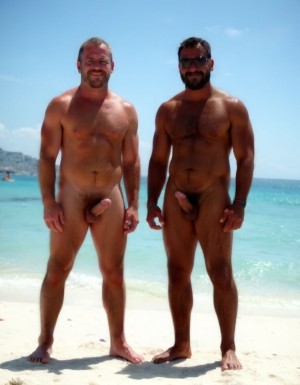 Rodrigo y Maximiliano son dos hombres culturistas de competición posando juntos en una playa de arena blanca con mar turquesa cristalino de fondo y cielo azul despejado, ambos descalzos sobre la arena, sonriendo a cámara con complicidad, postura relajada con las caderas pegadas y manos en la cintura.

Rodrigo es un hombre que está a la izquierda: caucásico de 35 años, cabeza completamente rapada y afeitada brillante por el sol, rostro cuadrado con mandíbula ancha, sonrisa amplia mostrando dientes blancos, cejas finas oscuras, ojos oscuros, piel bronceada aceitosa con brillo uniforme, cuello grueso de toro con trapecios enormes subiendo hasta las orejas, deltoides redondos y estriados como bolas de cañón con separación clara de las tres cabezas, pectorales masivos gruesos y cuadrados con estriaciones visibles en la parte inferior y surco profundo entre ambos, pezones pequeños apuntando hacia abajo por el volumen del pectoral, brazos enormes con bíceps con pico pronunciado y vena cefálica gruesa visible, tríceps con herradura marcada, antebrazos gruesos vascularizados, abdominales de seis bloques marcados con separaciones profundas, oblicuos definidos, serratos visibles, dorsales anchos que sobresalen por detrás dándole forma de V pronunciada, completamente desnudo de cintura para abajo, polla erecta de treinta y seis centímetros de longitud y ocho coma cinco centímetros de diámetro apuntando hacia arriba y ligeramente a la derecha, tronco grueso y venoso con venas retorcidas recorriéndolo desde la base hasta el glande, glande grande rosado hinchado y brillante completamente expuesto, testículos enormes gordos y pesados colgando bajos en un escroto relajado por el calor oscurecido por el bronceado, pubis recortado corto, muslos masivos con cuádriceps con forma de lágrima y separaciones marcadas, gemelos gruesos con forma de diamante, pies grandes sobre la arena.

Maximiliano es un hombre que está a la derecha: negro de piel oscura de 45 años, cabeza rapada al cero, rostro angular con pómulos altos y marcados, mandíbula cuadrada y definida, sonrisa confiada mostrando dientes blancos, ojos oscuros intensos, piel negra brillante y aceitada que resalta cada definición muscular con reflejos del sol, cuello grueso con trapecios altos, deltoides estriados enormes y redondos con venas cruzándolos, pectorales cuadrados duros y estriados con pezones oscuros pequeños, separación brutal entre ambos pectorales, brazos fibrosos masivos con bíceps vascularizados y venas gruesas serpenteando por todo el brazo, tríceps estriados con las tres cabezas visibles, antebrazos secos con cada tendón marcado, abdominales de ocho bloques profundamente tallados con piel fina pegada al músculo mostrando cada fibra, oblicuos cortados como cuchillas, serratos marcados individualmente, dorsales anchos y gruesos, completamente desnudo de cintura para abajo, polla erecta de treinta y seis centímetros de longitud y ocho coma cinco centímetros de diámetro con tronco oscuro grueso y pesado cubierto de venas hinchadas prominentes, glande enorme oscuro casi negro brillante de líquido preseminal, prepucio retraído por completo, testículos enormes gordos y llenos colgando pesados y bajos en un escroto oscuro arrugado y relajado, pubis con vello negro corto y rizado, muslos enormes fibrosos con cuádriceps estriados y femorales como cuerdas de acero, gemelos definidos y duros, pies descalzos sobre la arena blanca.

Iluminación natural directa del sol cenital con reflejos en la piel aceitada de Rodrigo y Maximiliano, sombras cortas en la arena, alta resolución fotográfica hiperrealista, textura de piel con poros visibles, gotas de sudor y aceite, calidad de fotografía profesional editorial deportiva, plano frontal de cuerpo entero.



No distorsiones y NO DEFORMACIONES.