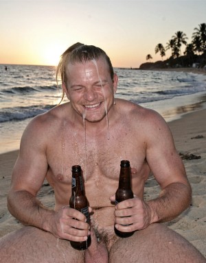 Un turista musculoso sale de una zona de cruising cercana a una playa, tiene restos de semen ya que ha recibido el bukakke que andaba buscando y lo celebra bebiendo cerveza y riendo, de rodillas sobre la arena.