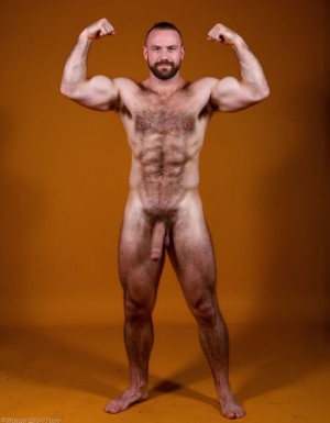 hombre culturista de 35 años posando desnudo de cuerpo completo, sonriente, tensa los bíceps, tiene un pene de 40 cm de longitud y 7 cm de diámetro, grandes dorsales, piernas, cintura estrecha, un poco calvo, grandes pezones rosas. Tiene un pene de 40 cm de longitud y 7 cm de diámetro. Tiene mucho vello en pecho y brazos y piernas. Tiene testículos de 10 kg de peso y están colgando. Tiene pies con sus uñas rojas. Fondo color amarando. Tiene el pene empalmado y eyaculando. 