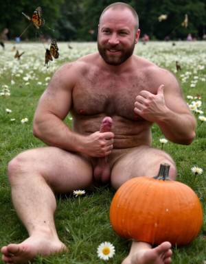hombre culturista de 35 años posando desnudo de cuerpo completo, sonriente, tensa los bíceps, tiene un pene de 40 cm de longitud y 7 cm de diámetro, tiene grandes dorsales, piernas, tiene cintura estrecha, es un poco calvo, tiene grandes pezones rosas. Tiene un pene de 40 cm de longitud y 7 cm de diámetro. Tiene mucho vello en pecho y brazos y piernas. Tiene testículos de 10 cm de diámetro que están colgando y se mueven al compás de los movimientos del cuerpo. Tiene pies con sus uñas pintadas de color rojo. Fondo de muchas margaritas de todos los colores y miles de mariposas volando. Tiene el cuerpo bronceado por el Sol. Está en la hierva rodeado de margaritas. Está sentado y quiere enseñar su ano. Tiene el ano relajado y abierto y a la vista del espectador. Por su pene erecto. Con su mano derecha rodea su pene por su perímetro acariciando el pene con suavidad. Hoy es Halloween y hay decoración de Halloween