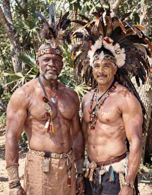 el jefe de la tribu apache con su guerrero favorito que le atrae y con el que mantiene relaciones sexuales, ambos completamente desnudos y musculosos ante otros hombres desnudos de la tribu. Llevan penachos de plumas y abalorios típicos de la tribu