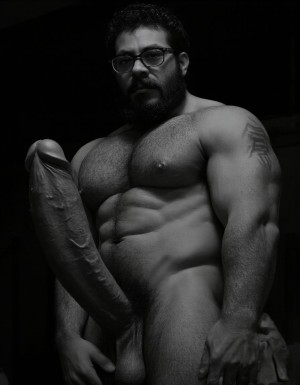 Fotografía hiperrealista en blanco y negro de un hombre adulto musculoso a la vista desde las rodillas para arriba hasta la cabeza, cuerpo muy delgado con musculación marcada y definida, rostro masculino, totalmente desnudo con polla erecta de treinta centímetros de longitud y ocho centímetros de diámetro, tiene rasgos marcados duros expresivos, barba densa poblada tupida oscura estilo hipster cubriendo completamente mandíbula mentón mejillas con grosor uniforme textura abundante muy definida, bigote denso tupido oscuro conectado perfectamente con la barba completa cubriendo completamente el labio superior, pelo oscuro medio peinado completamente recto hacia arriba con volumen considerable estilo hipster moderno quiff puntas verticales texturizadas hacia el cielo con altura prominente, cejas gruesas oscuras pobladas muy marcadas definidas, gafas de montura completa negra cuadradas grandes estilo hipster moderno sobre el puente de la nariz enmarcando unos ojos oscuros intensos que miran directamente a cámara con expresión seria penetrante confiada, expresión facial seria masculina sin sonrisa con mirada directa desafiante, pómulos marcados definidos angulares, nariz recta proporcionada, labios medios apenas visibles completamente cubiertos por bigote denso que conecta con la barba hipster completa, torso desnudo muy musculoso con pectorales enormes desarrollados y definidos, hombros anchos musculosos deltoide prominentes, brazos musculosos gruesos con bíceps y tríceps marcados visibles a ambos lados del cuerpo, abdomen tonificado marcado visible desde la cintura, piel con textura realista detallada poros imperfecciones sutiles, vello corporal denso oscuro abundante cubriendo pectorales abdomen brazos hombros con textura natural masculina muy visible, tatuaje en tinta negra en el bíceps del brazo derecho con la palabra exacta "hipsterbarba" en tipografía negra sans-serif clara legible tatuada sobre la piel del brazo de tamaño mediano visible proporcionado, iluminación dramática lateral direccional que crea contraste alto marcado entre luces brillantes y sombras profundas resaltando la estructura facial angular la barba hipster densa las gafas cuadradas grandes el vello corporal abundante la musculatura del torso los brazos y en el bíceps derecho tiene un tatuaje con la palabra a la vista: "hipsterbarba", fondo completamente oscuro negro liso uniforme desenfocado sin distracciones, fotografía analógica en blanco y negro de alto contraste con grano fotográfico sutil visible estilo retrato hipster masculino fitness, enfoque nítido absoluto perfecto en el rostro especialmente en los ojos detrás de las gafas la barba hipster densa el bigote tupido el pelo vertical el vello corporal el torso musculoso y el tatuaje en el brazo derecho con la palabra a la vista "hipsterbarba", encuadre vertical desde las rodillas cintura hacia arriba mostrando pene erecto de treinta centímetros de longitud completamente todo el torso superior los brazos musculosos y la cabeza, calidad fotográfica hiperrealista 8K máxima definición detalle extremo, renderizado cinematográfico fotorrealista profesional.