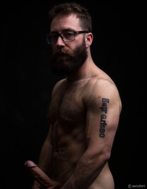 Fotografía hiperrealista de un hombre adulto musculoso a la vista desde las rodillas para arriba hasta la cabeza, rostro masculino idéntico a la imagen de referencia totalmente desnudo con polla erecta de treinta centímetros de longitud y ocho centímetros de diámetro, tiene rasgos marcados duros expresivos, barba densa poblada tupida oscura estilo hipster cubriendo completamente mandíbula mentón mejillas con grosor uniforme textura abundante muy definida, bigote denso tupido oscuro conectado perfectamente con la barba completa cubriendo completamente el labio superior, pelo oscuro medio peinado completamente recto hacia arriba con volumen considerable estilo hipster moderno quiff puntas verticales texturizadas hacia el cielo con altura prominente, cejas gruesas oscuras pobladas muy marcadas definidas, gafas de montura completa negra cuadradas grandes estilo hipster moderno sobre el puente de la nariz enmarcando unos ojos oscuros intensos que miran directamente a cámara con expresión seria penetrante confiada, expresión facial seria masculina sin sonrisa con mirada directa desafiante, pómulos marcados definidos angulares, nariz recta proporcionada, labios medios apenas visibles completamente cubiertos por bigote denso que conecta con la barba hipster completa, torso desnudo muy musculoso con pectorales enormes desarrollados y definidos y velludos peludos, hombros anchos musculosos deltoide prominentes, brazos musculosos gruesos con bíceps y tríceps marcados visibles a ambos lados del cuerpo, abdomen tonificado marcado visible desde la cintura, piel con textura realista detallada poros imperfecciones sutiles, vello corporal denso oscuro abundante cubriendo pectorales abdomen brazos hombros con textura natural masculina muy visible, tatuaje en tinta negra en el bíceps del brazo derecho con la palabra exacta (("hipsterbarba")) en tipografía negra sans-serif clara legible tatuada sobre la piel del brazo de tamaño mediano visible proporcionado, iluminación dramática lateral direccional que crea contraste alto marcado entre luces brillantes y sombras profundas resaltando la estructura facial angular la barba hipster densa las gafas cuadradas grandes el vello corporal abundante la musculatura del torso los brazos y el tatuaje con la palabra (("hipsterbarba")) en el bíceps derecho, fondo completamente oscuro negro liso uniforme desenfocado sin distracciones, fotografía de alto contraste con grano fotográfico sutil visible estilo retrato hipster masculino fitness, enfoque nítido absoluto perfecto en el rostro especialmente en los ojos detrás de las gafas la barba hipster densa el bigote tupido el pelo vertical el vello corporal el torso musculoso y el tatuaje con la palabra (("hipsterbarba")) en el brazo derecho, encuadre vertical desde la cintura hacia arriba mostrando completamente todo el torso superior los brazos musculosos y la cabeza, calidad fotográfica hiperrealista 8K máxima definición detalle extremo, renderizado cinematográfico fotorrealista profesional. Está totalmente desnudo.