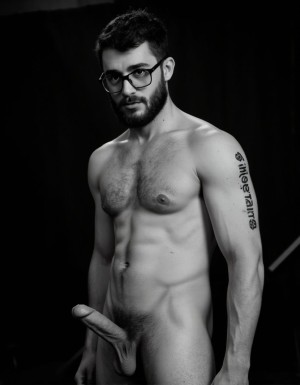 Fotografía hiperrealista en blanco y negro de un hombre adulto musculoso a la vista desde las rodillas para arriba hasta la cabeza, cuerpo muy delgado con musculación marcada y definida, rostro masculino, totalmente desnudo con polla erecta de treinta centímetros de longitud y ocho centímetros de diámetro, tiene rasgos marcados duros expresivos, barba densa poblada tupida oscura estilo hipster cubriendo completamente mandíbula mentón mejillas con grosor uniforme textura abundante muy definida, bigote denso tupido oscuro conectado perfectamente con la barba completa cubriendo completamente el labio superior, pelo oscuro medio peinado completamente recto hacia arriba con volumen considerable estilo hipster moderno quiff puntas verticales texturizadas hacia el cielo con altura prominente, cejas gruesas oscuras pobladas muy marcadas definidas, gafas de montura completa negra cuadradas grandes estilo hipster moderno sobre el puente de la nariz enmarcando unos ojos oscuros intensos que miran directamente a cámara con expresión seria penetrante confiada, expresión facial seria masculina sin sonrisa con mirada directa desafiante, pómulos marcados definidos angulares, nariz recta proporcionada, labios medios apenas visibles completamente cubiertos por bigote denso que conecta con la barba hipster completa, torso desnudo muy musculoso con pectorales enormes desarrollados y definidos, hombros anchos musculosos deltoide prominentes, brazos musculosos gruesos con bíceps y tríceps marcados visibles a ambos lados del cuerpo, abdomen tonificado marcado visible desde la cintura, piel con textura realista detallada poros imperfecciones sutiles, vello corporal denso oscuro abundante cubriendo pectorales abdomen brazos hombros con textura natural masculina muy visible, tatuaje en tinta negra en el bíceps del brazo derecho con la palabra exacta "hipsterbarba" en tipografía negra sans-serif clara legible tatuada sobre la piel del brazo de tamaño mediano visible proporcionado, iluminación dramática lateral direccional que crea contraste alto marcado entre luces brillantes y sombras profundas resaltando la estructura facial angular la barba hipster densa las gafas cuadradas grandes el vello corporal abundante la musculatura del torso los brazos y en el bíceps derecho tiene un tatuaje con la palabra a la vista: "hipsterbarba", fondo completamente oscuro negro liso uniforme desenfocado sin distracciones, fotografía analógica en blanco y negro de alto contraste con grano fotográfico sutil visible estilo retrato hipster masculino fitness, enfoque nítido absoluto perfecto en el rostro especialmente en los ojos detrás de las gafas la barba hipster densa el bigote tupido el pelo vertical el vello corporal el torso musculoso y el tatuaje en el brazo derecho con la palabra a la vista "hipsterbarba", encuadre vertical desde las rodillas cintura hacia arriba mostrando pene erecto de treinta centímetros de longitud completamente todo el torso superior los brazos musculosos y la cabeza, calidad fotográfica hiperrealista 8K máxima definición detalle extremo, renderizado cinematográfico fotorrealista profesional.