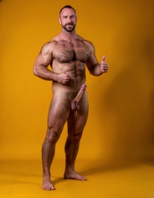 hombre culturista de 35 años posando desnudo de cuerpo completo, sonriente, tensa los bíceps, tiene un pene de 40 cm de longitud y 7 cm de diámetro, grandes dorsales, piernas, cintura estrecha, un poco calvo, grandes pezones rosas. Tiene un pene de 40 cm de longitud y 7 cm de diámetro. Tiene mucho vello en pecho y brazos y piernas. Tiene testículos de 10 kg de peso y están colgando. Tiene pies con sus uñas rojas. Fondo amarillo oscuro.
