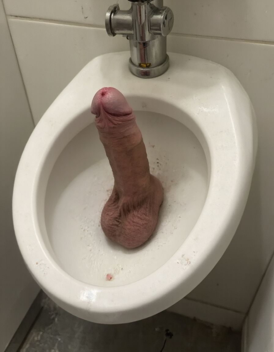 Dildos. Imagen surrealista, alguien ha colocado un consolador (dildo) de color carne y muy perfecto en un urinario público, un chico hetero lo mira con asco. 