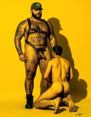 Dibujo realista. Amo barbudo tatuado e hiper masculino, muy musculoso pero muy delgado, con arnés. Tiene un gran pene eyaculando. Lleva gorra militar y unos anillos en los pezones, Un esclavo de rodillas. Respeta la forma y la proporción del cuerpo y se fiel a la forma real sin distorsiones. Fondo amarillo oscuro con los reflejos de las sombras de los cuerpos del amo y el esclavo.