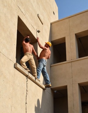dos obreros de la construcción descamisados por el calor,  trabajan juntos en un edificio alto, a pesar de la situación, uno le mete la mano al otro por debajo del pantalón. 