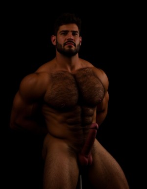 Arturo. Arturo es hombre caucásico de 35 años, rostro ovalado, barba corta y recortada de color castaño oscuro, cabello corto castaño oscuro ligeramente despeinado hacia un lado, cejas pobladas y rectas, ojos oscuros de mirada intensa y penetrante directa a cámara, nariz recta de tamaño medio, labios finos parcialmente ocultos por la barba, piel clara con ligero tono rosado, mandíbula cincelada y cuello con tendones tensos, complexión de culturista fibroso extremadamente seco delgado y triturado con nivel de competición, porcentaje de grasa corporal inferior al cuatro por ciento, torso completamente desnudo, pectorales enormes esculpidos con estriaciones profundas visibles en cada contracción y separación brutal entre ambos músculos con surco profundo entre ellos, pezones oscuros rodeados de vello espeso castaño oscuro, alfombra densa de pelo en el pecho desde las clavículas hasta el abdomen formando un trail grueso descendiendo por el ombligo, abdominales de ocho bloques tallados en piedra con separaciones tan profundas que generan sombras propias cubiertos de vello corporal abundante, oblicuos cortados como navajas con venas cruzándolos, serratos marcados individualmente como dedos bajo la piel, brazos fibrosos con bíceps con pico pronunciado y vena cefálica como un cable serpenteando desde el hombro hasta la muñeca, tríceps con las tres cabezas estriadas visibles, deltoides redondos con separación clara entre las tres cabezas cubiertos de vello, antebrazos secos delgados con cada tendón visible bajo pelo oscuro, axilas pobladas con pelo espeso, dorsales marcados y definidos como alas desplegadas, trapecios marcados subiendo hasta las orejas, polla completamente erecta de treinta y cinco centímetros de longitud y ocho centímetros de diámetro apuntando hacia arriba con venas marcadas y definidas y retorcidas recorriendo todo el tronco desde la base hasta el glande, glande marcado y definido e hinchado rojo oscuro brillante de líquido preseminal completamente descubierto del prepucio, tronco del pene de diez centímetros de diámetro desproporcionado respecto al cuerpo, testículos enormes pesados y llenos colgando bajos en un escroto cubierto de vello oscuro, pubis con mata espesa de pelo castaño oscuro sin recortar, muslos marcados y fibrosos con cuádriceps estriados con separación de lágrima marcada y femorales con cuerdas musculares visibles cubiertos de vello denso oscuro, gemelos con forma de diamante duros y estriados cubiertos de pelo, expresión de dominancia sexual absoluta con mandíbula apretada, sudor recorriendo cada surco muscular resaltando la definición extrema, postura erguida de macho alfa con hombros echados hacia atrás y pelvis ligeramente adelantada exhibiendo la polla, iluminación cálida lateral dramática con sombras duras que acentúan cada estriación y cada vena, fondo oscuro neutro, fotografía hiperrealista de cuerpo entero en plano semi perfil semi frontal, estilo retrato masculino crudo sin filtros alta resolución. Antes de crear esta imagen repite la lectura de este texto tres veces, antes de crear la imagen. No distorsiones y NO DEFORMACIONES.