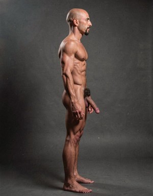 Mike Morris, a 32-year-old extremely lean Caucasian male with only 8% body fat, stands completely naked in a rigid military attention pose captured in a full-body exact side profile at 90 degrees from his right side. The shot runs uninterrupted from the tips of his size 44 slightly hairy feet all the way up to the top of his bald head, showing his entire body without any cropping whatsoever. His physique is dry, highly vascular and powerfully defined: massive square pectorals seen in perfect side silhouette, dense dark brown chest hair forming a thick T-pattern that continues across his shoulders and back, sharply carved six-pack abs in clear profile, narrow waist, wide flaring lats, powerful thighs and diamond-shaped calves covered in the same dark hair. Dramatic directional studio lighting falls from high and slightly in front of him, creating strong rim lighting that traces every sharp edge of his muscular outline, accentuating the texture of his dense dark body hair on chest, shoulders, lower back, ass and legs, while producing deep shadows that highlight every muscle separation, vein and the extreme dryness of his 8% body fat. His advanced Norwood III-IV bald scalp is clearly visible under the light, with very short dense dark brown hair only on the sides and back of his head. His square, angular face is shown in pure right profile: strong jawline, prominent chin with slight central dimple, thick well-groomed dark handlebar mustache, heavy brow and intense deep-set brown eye staring straight forward with a serious, commanding expression. His penis is fully and clearly visible in perfect side view, completely natural and anatomically correct: thick, 24 cm long when fully erect, with a natural slight upward curve, prominent dorsal veins running along the shaft, long foreskin that partially covers the pink-red glans, and noticeably lighter skin tone than the rest of his bronzed body. Below it hang his large, low-hanging testicles with wrinkled darker skin and an extremely dense, curly dark brown pubic bush that climbs almost to his navel and surrounds the base of his cock and balls generously. Every detail from his veined hands and forearms to his muscular ass, hamstrings, diamond calves and hairy toes is perfectly proportioned and free of any deformation. Photorealistic, high-contrast, masculine 1970s Colt Studio aesthetic with subtle grainy film texture.