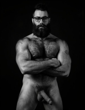 Fotografía hiperrealista en blanco y negro de un hombre adulto musculoso a la vista desde las rodillas para arriba hasta la cabeza, cuerpo muy delgado con musculación marcada y definida, rostro masculino, totalmente desnudo con polla erecta de treinta centímetros de longitud y ocho centímetros de diámetro, tiene rasgos marcados duros expresivos, barba densa poblada tupida oscura estilo hipster cubriendo completamente mandíbula mentón mejillas con grosor uniforme textura abundante muy definida, bigote denso tupido oscuro conectado perfectamente con la barba completa cubriendo completamente el labio superior, pelo oscuro medio peinado completamente recto hacia arriba con volumen considerable estilo hipster moderno quiff puntas verticales texturizadas hacia el cielo con altura prominente, cejas gruesas oscuras pobladas muy marcadas definidas, gafas de montura completa negra cuadradas grandes estilo hipster moderno sobre el puente de la nariz enmarcando unos ojos oscuros intensos que miran directamente a cámara con expresión seria penetrante confiada, expresión facial seria masculina sin sonrisa con mirada directa desafiante, pómulos marcados definidos angulares, nariz recta proporcionada, labios medios apenas visibles completamente cubiertos por bigote denso que conecta con la barba hipster completa, torso desnudo muy musculoso con pectorales enormes desarrollados y definidos, hombros anchos musculosos deltoide prominentes, brazos musculosos gruesos con bíceps y tríceps marcados visibles a ambos lados del cuerpo, abdomen tonificado marcado visible desde la cintura, piel con textura realista detallada poros imperfecciones sutiles, vello corporal denso oscuro abundante cubriendo pectorales abdomen brazos hombros con textura natural masculina muy visible, tatuaje en tinta negra en el bíceps del brazo derecho con la palabra exacta "hipsterbarba" en tipografía negra sans-serif clara legible tatuada sobre la piel del brazo de tamaño mediano visible proporcionado, iluminación dramática lateral direccional que crea contraste alto marcado entre luces brillantes y sombras profundas resaltando la estructura facial angular la barba hipster densa las gafas cuadradas grandes el vello corporal abundante la musculatura del torso los brazos y el tatuaje con la palabra ((hipsterbarba)) en el bíceps derecho, fondo completamente oscuro negro liso uniforme desenfocado sin distracciones, fotografía analógica en blanco y negro de alto contraste con grano fotográfico sutil visible estilo retrato hipster masculino fitness, enfoque nítido absoluto perfecto en el rostro especialmente en los ojos detrás de las gafas la barba hipster densa el bigote tupido el pelo vertical el vello corporal el torso musculoso y el tatuaje con la palabra "hipsterbarba" en el brazo derecho, encuadre vertical desde las rodillas cintura hacia arriba mostrando pene erecto de treinta centímetros de longitud completamente todo el torso superior los brazos musculosos y la cabeza, calidad fotográfica hiperrealista 8K máxima definición detalle extremo, renderizado cinematográfico fotorrealista profesional.