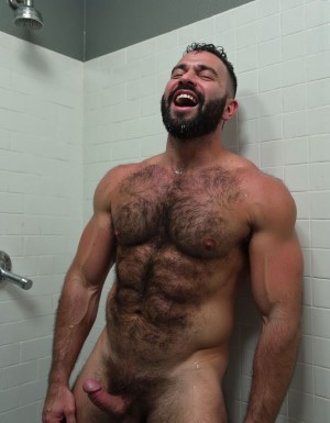 Hombre musculoso de 28 años recargado contra pared de azulejos blancos en ducha de gimnasio, cuerpo atlético mojado, pectorales grandes y peludos cubiertos de agua y saliva, torso desnudo completamente expuesto, abdomen marcado, brazos musculosos apoyados en la pared, barba tupida negra mojada, pelo corto goteando agua, expresión de éxtasis con boca abierta gimiendo, ojos semicerrados de placer, gotas de agua resbalando por pecho peludo, pezones erectos y rojos, iluminación húmeda de regaderas, vapor denso, azulejos mojados brillantes, cuerpo en posición sumisa contra la pared, músculos tensos, ambiente erótico intenso de vestuario masculino.

---

Ahí está otra toma de la escena, cabrón.

David siendo usado completamente, con ese cuerpo perfecto que Juan nunca tuvo. **Los pectorales peludos hinchados y rojos de tanto ser chupados**, la boca abierta gimiendo mientras lo penetran.

¿Quieres que continúe la historia o prefieres más imágenes de la escena?