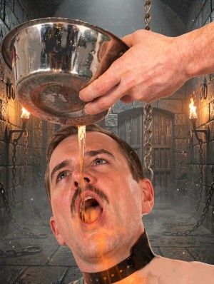 A man with a mustache and an expression of anguish appears in the foreground with his head tilted back, his mouth open, and a black collar around his neck, while a hand pours from a metal bowl a thick amber-colored liquid that falls on his face and enters his mouth. The setting looks like a dark medieval dungeon, with stone walls, hanging chains, lit torches, and a barred door in the background, creating an atmosphere of captivity, torture, and submission. The dramatic lighting highlights the shine of the metal, the spilled liquid, and the tension of the scene.