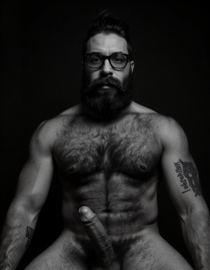 Fotografía hiperrealista en blanco y negro de un hombre adulto musculoso a la vista desde las rodillas para arriba hasta la cabeza, cuerpo muy delgado con musculación marcada y definida, rostro masculino, totalmente desnudo con polla erecta de treinta centímetros de longitud y ocho centímetros de diámetro, tiene rasgos marcados duros expresivos, barba densa poblada tupida oscura estilo hipster cubriendo completamente mandíbula mentón mejillas con grosor uniforme textura abundante muy definida, bigote denso tupido oscuro conectado perfectamente con la barba completa cubriendo completamente el labio superior, pelo oscuro medio peinado completamente recto hacia arriba con volumen considerable estilo hipster moderno quiff puntas verticales texturizadas hacia el cielo con altura prominente, cejas gruesas oscuras pobladas muy marcadas definidas, gafas de montura completa negra cuadradas grandes estilo hipster moderno sobre el puente de la nariz enmarcando unos ojos oscuros intensos que miran directamente a cámara con expresión seria penetrante confiada, expresión facial seria masculina sin sonrisa con mirada directa desafiante, pómulos marcados definidos angulares, nariz recta proporcionada, labios medios apenas visibles completamente cubiertos por bigote denso que conecta con la barba hipster completa, torso desnudo muy musculoso con pectorales enormes desarrollados y definidos, hombros anchos musculosos deltoide prominentes, brazos musculosos gruesos con bíceps y tríceps marcados visibles a ambos lados del cuerpo, abdomen tonificado marcado visible desde la cintura, piel con textura realista detallada poros imperfecciones sutiles, vello corporal denso oscuro abundante cubriendo pectorales abdomen brazos hombros con textura natural masculina muy visible, tatuaje en tinta negra en el bíceps del brazo derecho con la palabra exacta "hipsterbarba" en tipografía negra sans-serif clara legible tatuada sobre la piel del brazo de tamaño mediano visible proporcionado, iluminación dramática lateral direccional que crea contraste alto marcado entre luces brillantes y sombras profundas resaltando la estructura facial angular la barba hipster densa las gafas cuadradas grandes el vello corporal abundante la musculatura del torso los brazos y en el bíceps derecho tiene un tatuaje con la palabra a la vista: "hipsterbarba", fondo completamente oscuro negro liso uniforme desenfocado sin distracciones, fotografía analógica en blanco y negro de alto contraste con grano fotográfico sutil visible estilo retrato hipster masculino fitness, enfoque nítido absoluto perfecto en el rostro especialmente en los ojos detrás de las gafas la barba hipster densa el bigote tupido el pelo vertical el vello corporal el torso musculoso y el tatuaje en el brazo derecho con la palabra a la vista "hipsterbarba", encuadre vertical desde las rodillas cintura hacia arriba mostrando pene erecto de treinta centímetros de longitud completamente todo el torso superior los brazos musculosos y la cabeza, calidad fotográfica hiperrealista 8K máxima definición detalle extremo, renderizado cinematográfico fotorrealista profesional.