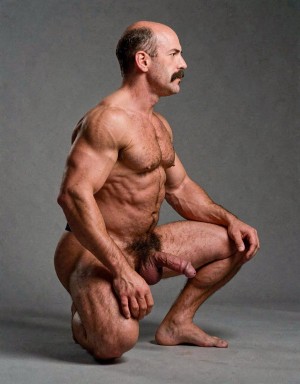 Hombre desnudo de perfil arrodillado en un estudio de fondo gris neutro, con una postura serena y escultórica que resalta su musculatura marcada en hombros, brazos, pecho, abdomen y piernas. Tiene la cabeza parcialmente calva, pelo oscuro en los laterales y un bigote espeso, mirando hacia la derecha con expresión concentrada. Una rodilla apoya en el suelo mientras la otra pierna queda flexionada, con las manos relajadas sobre el muslo y la rodilla. El vello corporal es visible en el pecho, el abdomen y el pubis, y el pene queda claramente expuesto en una composición de desnudo masculino artístico, sobria y centrada en la anatomía.