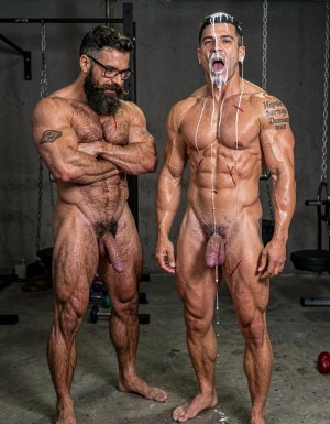 Hyperrealistic cinematic photograph, full body frontal view, perfect anatomy and proportions with zero distortions. Dark brutal dungeon gym with concrete floor, hanging chains and BDSM equipment softly blurred in the background. Dramatic side lighting, high contrast, sweat and cum glistening on skin.

Hipsterbarba stands on the left, 40 years old, 180cm, 80kg, 8% body fat, powerful muscle bear physique completely naked and covered in dense dark body hair on chest, shoulders, abs and thighs. Long thick Bandholz beard, curled handlebar mustache, black glasses, arms crossed, dominant and satisfied expression while looking down at your slave.

Anil stands right in front of you, 25 years old, extreme bodybuilder slave, 175cm, 80kg, 6% body fat, completely smooth tanned skin from the neck down. Massive 127cm chest, eight-pack abs with fresh red whip marks, 47cm veiny arms, tiny 60cm waist, wide V-taper, round 90cm glutes and 70cm quads. He stands at full attention, head up, staring directly into your eyes with pure submissive adoration and fear. His mouth is wide open, tongue slightly out, completely covered in thick white cum: heavy ropes of semen dripping from his forehead, eyebrows, nose, cheeks, lips and chin, running down onto his huge pecs. The metal cock ring is tight around the base of his swollen, purple, semi-hard cock that leaks a long string of precum onto the concrete floor. Fresh whip marks across his shoulders and abs. The tattoo 