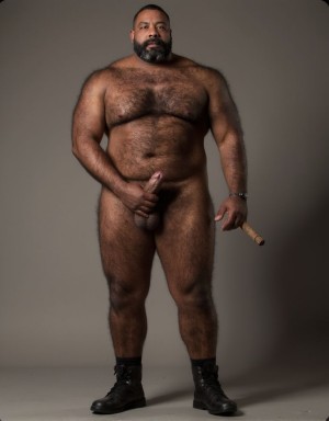 Retrato de un señor de 50 años alto y de complexión fuerte con barriga abultada, piel morena y todo el cuerpo cubierto de pelo, con su mano derecha sujeta su pene erecto que mide más de 24 centímetros. El hombre viste solamente unas botas de cuero negro. En la otra mano sostiene un puro