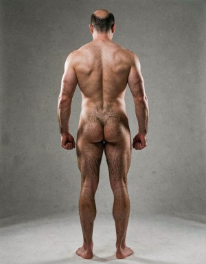 Mike Morris, a 32-year-old extremely lean Caucasian male at only 8% body fat, stands completely naked in a strict military attention pose seen from directly behind in a full posterior view. His back is perfectly straight, shoulders pulled back, arms rigid at his sides with fists clenched, legs straight and together, head held high. The shot captures him from the heels of his feet all the way up to the top of his bald head. His advanced Norwood III-IV baldness is clearly visible from behind, with a smooth tanned scalp on the crown and short dense dark brown hair only on the sides and lower back of the head. His back is highly defined and vascular: wide lats tapering dramatically to a very narrow, tight waist, thick trapezius muscles, and dense dark brown body hair lightly covering the shoulders and becoming much thicker and denser across the lower back and lumbar area, especially between the lats. His ass is tight, muscular and round with almost no fat, the glutes clearly separated. Thick dark hair continues down onto his powerful diamond-shaped calves and the backs of his slightly hairy feet. Dramatic directional studio lighting from above and slightly to the side creates strong highlights on his dry, shredded skin and deep shadows that accentuate every muscle fiber, the texture of his dense back hair, and the extreme vascularity and definition of his 8% body fat physique. Photorealistic, high-contrast, masculine 1970s Colt Studio aesthetic, grainy film texture, commanding and powerful presence. Las piernas están separadas 80 cm. La separación entre los pies es de ochenta centímetros. Se aprecia el surco entre glúteos  con una separación de glúteos de 2 cm.