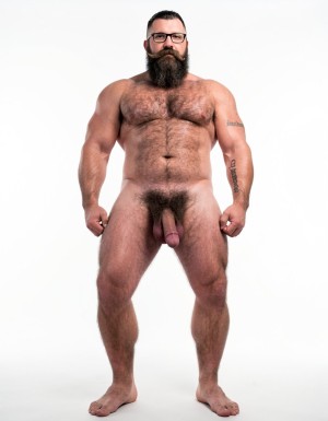 A highly detailed full-body nude photograph of Hipsterbarba, a 40-year-old muscle bear master, standing completely naked from head to toe in a bright white photography studio with perfect even lighting. He is exactly 180cm tall, 80kg with 8% body fat, strong and athletic physique. Massive rounded pecs, very defined six-pack abs, wide shoulders, thick vascular arms, powerful legs, wide V-shaped back. Dense dark body hair covering his chest, shoulders, abs, thick pubic bush and thighs. High fade undercut haircut, very thick long Bandholz beard that reaches almost to his chest, thick curled handlebar mustache with spiral ends, black-rimmed glasses. Small tattoo on his right arm that says “hipsterbarba”. Thick cock with partial foreskin and visible pink glans, heavy low-hanging balls. Serious dominant expression, bare feet on the floor, full body view from head to toes, ultra realistic skin texture, dense body hair details, professional studio photography.