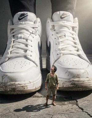 A terrified 50-year-old Spanish man shrunk down to insect size, standing helplessly next to massive white Nike sneakers that tower over him like skyscrapers. The tiny man has dark hair with some gray, olive Mediterranean skin, wearing torn clothing from the shrinking process. He's looking up in fear and submission at the enormous sneakers, which show wear marks and dirt on the soles. The perspective emphasizes the extreme size difference - the man is barely the size of a shoelace eyelet. Dramatic lighting casts long shadows from the giant sneakers over the microscopic figure. Hyperrealistic, detailed, cinematic lighting, ground level perspective.