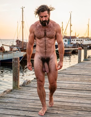 Ultra photorealistic 32k museum quality, cinematic golden hour lighting over the sea, perfect anatomy and proportions with zero distortion. Full body shot of Gayon Von Neumann walking alone on an old wooden pier at the maritime port. He is completely naked, 45 years old, 1.85m, 82kg, 4% body fat, brutally muscular and extremely hairy with thick black body hair covering his powerful chest, abs, arms and legs. Thick well-groomed black mustache, dense joined eyebrows, small intense dark eyes red from crying. His face shows deep sadness and loneliness, tears still running down his hard rural cheeks. He walks slowly with his head slightly down and shoulders a bit slumped, his massive 26cm thick veined cock hanging heavy and low between his powerful hairy legs, big low-hanging balls swinging with each step. The wind from the sea moves his body hair. Background of old fishing boats, calm sea and golden sunset light. Hyperrealistic skin texture, visible tears, detailed black body hair, natural sweat and sea wind effect, maximum realism, no surrealism, no deformation.