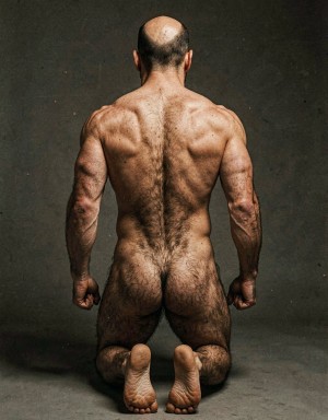 Mike Morris, a 32-year-old extremely lean Caucasian male at only 8% body fat, stands completely naked in a strict military attention pose seen from directly behind in a full posterior view. His back is perfectly straight, shoulders pulled back, arms rigid at his sides with fists clenched, legs straight and together, head held high. The shot captures him from the heels of his feet all the way up to the top of his bald head. His advanced Norwood III-IV baldness is clearly visible from behind, with a smooth tanned scalp on the crown and short dense dark brown hair only on the sides and lower back of the head. His back is highly defined and vascular: wide lats tapering dramatically to a very narrow, tight waist, thick trapezius muscles, and dense dark brown body hair lightly covering the shoulders and becoming much thicker and denser across the lower back and lumbar area, especially between the lats. His ass is tight, muscular and round with almost no fat, the glutes clearly separated. Thick dark hair continues down onto his powerful diamond-shaped calves and the backs of his slightly hairy feet. Dramatic directional studio lighting from above and slightly to the side creates strong highlights on his dry, shredded skin and deep shadows that accentuate every muscle fiber, the texture of his dense back hair, and the extreme vascularity and definition of his 8% body fat physique. Photorealistic, high-contrast, masculine 1970s Colt Studio aesthetic, grainy film texture, commanding and powerful presence.   Se aprecia el surco entre glúteos respingones  muy abierto con una separación de 4 centímetros entre glúteos. Está de rodillas.