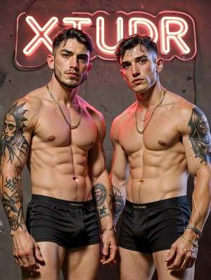Dos hombres musculosos posan de pie frente a una pared gris con un letrero de neón rojo que ilumina la escena y proyecta reflejos cálidos sobre sus cuerpos. Ambos están sin camiseta, llevan bóxers negros ajustados con cinturilla marcada y cadenas doradas al cuello, mostrando abdominales definidos, pecho trabajado y brazos tatuados. El hombre de la izquierda tiene barba corta, pelo oscuro peinado hacia atrás y tatuajes grandes en el brazo; el de la derecha luce el pelo húmedo y varios tatuajes en el hombro y el brazo. La composición tiene estética de estudio, moda masculina, fitness y ropa interior.